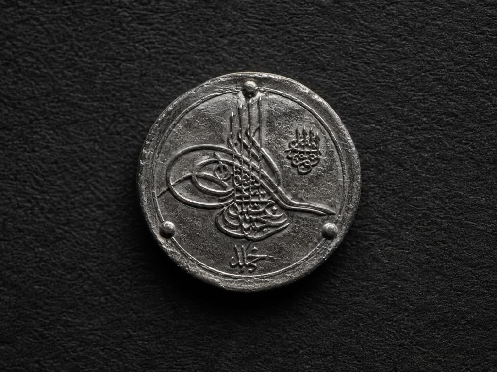 An Ottoman silver coin bearing a tughra calligraphic seal, side-lit.